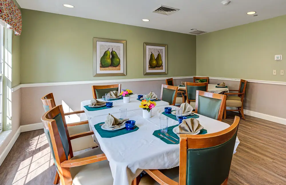 Allentown14 Dining room with a table set for six, featuring wooden chairs, white tablecloth, blue dishes, and flower centerpieces; framed pear art hangs on light green walls.