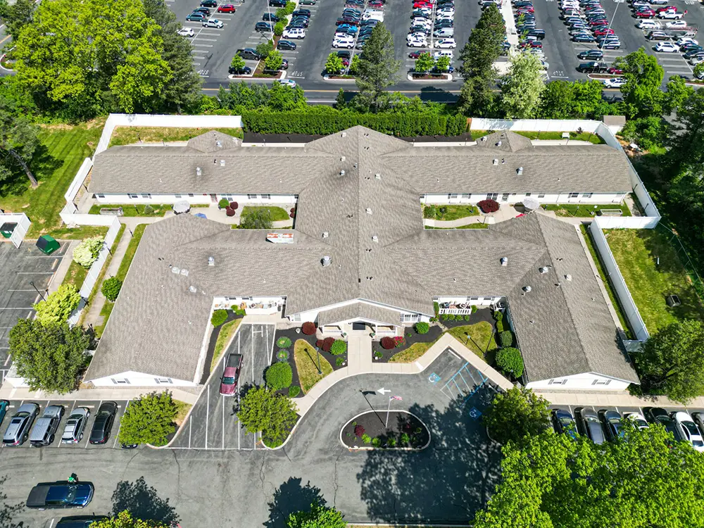 Allentown22 Aerial view of a single-story building with a landscaped entrance, adjacent parking lots, and a large parking area with many cars in the background.