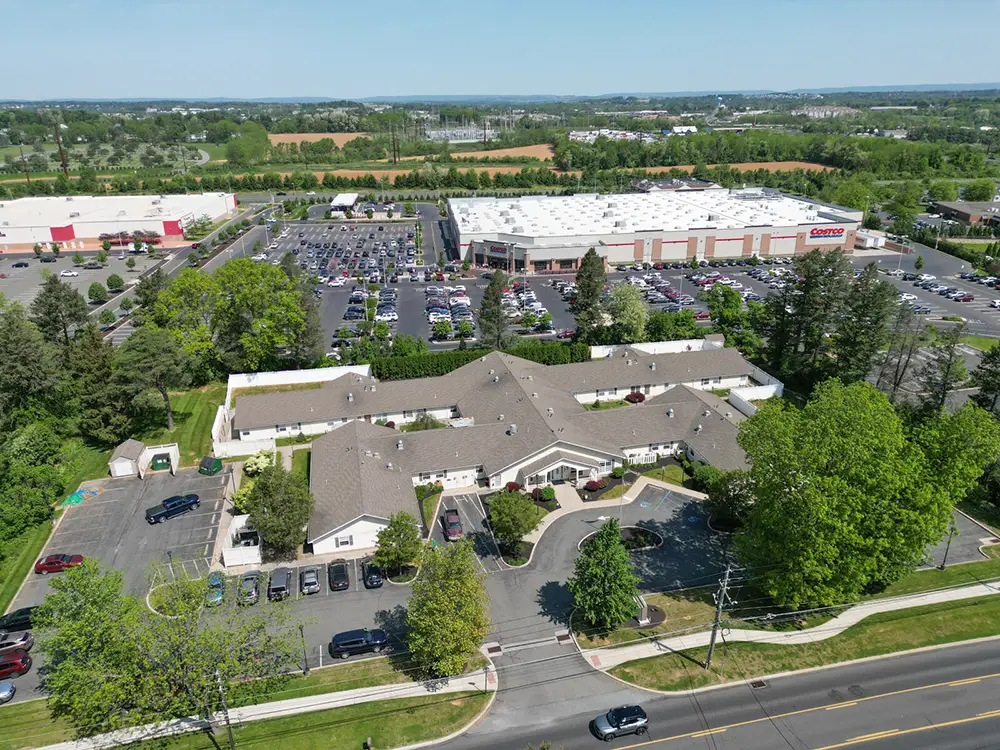 Allentown23 Aerial view of a commercial area with a large Costco warehouse, a parking lot filled with cars, and nearby buildings surrounded by trees and roads.