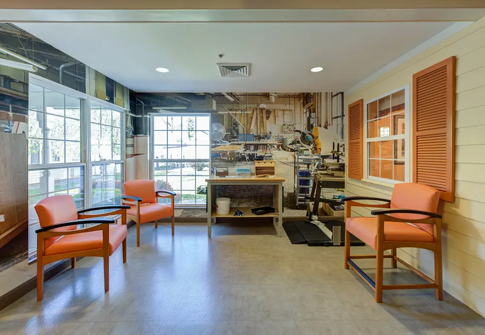 Allentown32 A waiting area with four orange chairs, large windows, and a mural of a woodworking shop on the back wall.