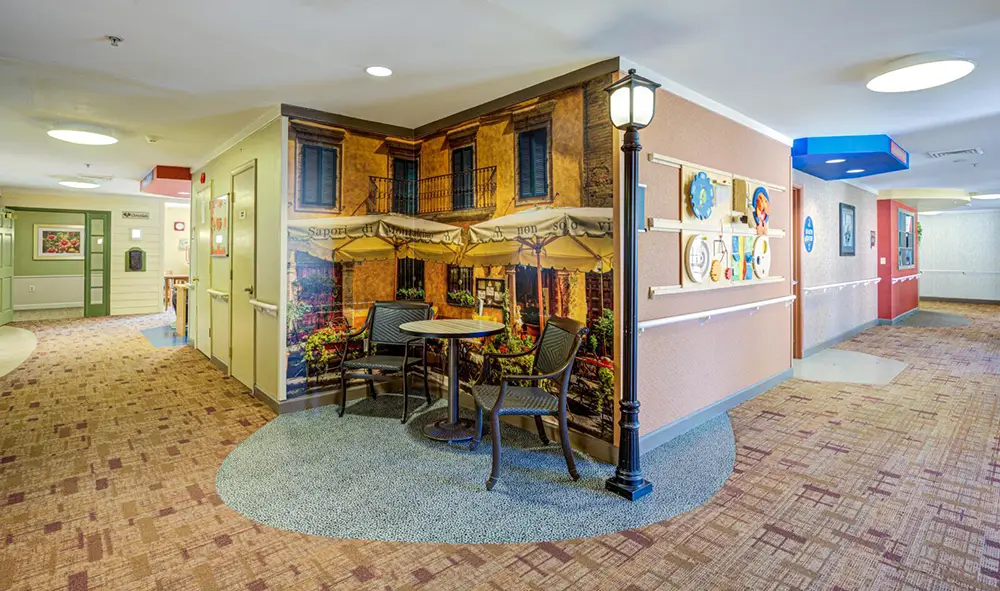Allentown33 A hallway with a mural of an outdoor cafe, a round table with two chairs, and a decorative streetlamp, creating a cozy, themed seating area.