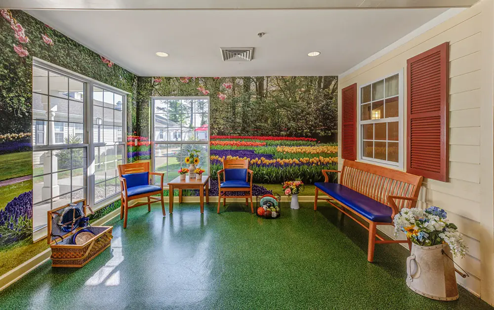 Allentown36 A waiting room with wooden benches and chairs, green flooring, flower arrangements, and a wall mural of a garden with tulips and trees.