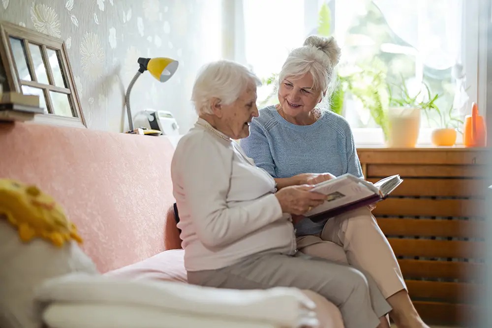 Two elderly women sit on a sofa, looking at a photo album together in a bright living room. Two elderly women sit on a sofa, looking at a photo album together in a bright living room.