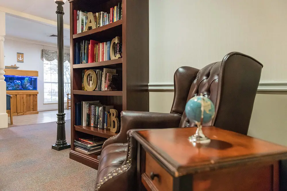 A brown leather armchair sits next to a small wooden table with a globe, beside a bookshelf filled with books in a warmly lit room. A brown leather armchair sits next to a small wooden table with a globe, beside a bookshelf filled with books in a warmly lit room.