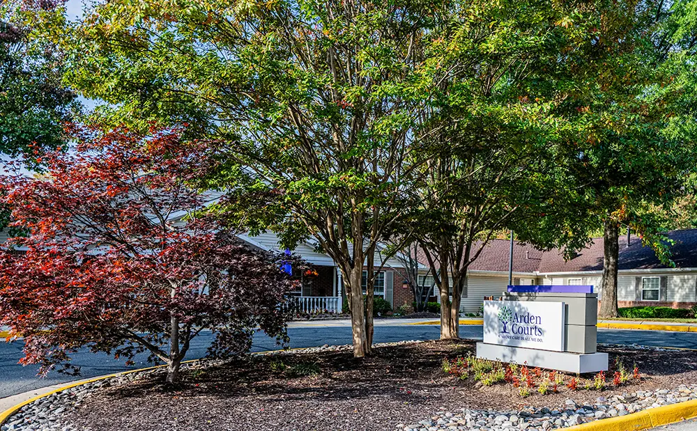 Fair Oaks A landscaped roundabout with trees and a sign that reads “Arden Courts” in front of a brick building with a covered porch.