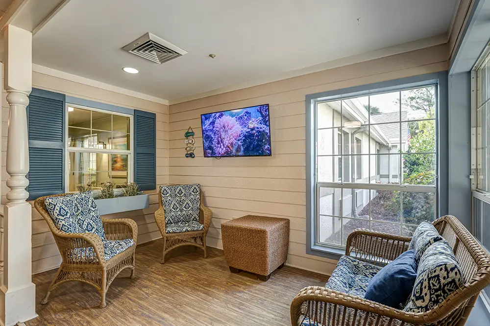 Small sunroom with wicker chairs, a wicker sofa, patterned cushions, a wall-mounted TV, large windows, and wood-style flooring. Small sunroom with wicker chairs, a wicker sofa, patterned cushions, a wall-mounted TV, large windows, and wood-style flooring.