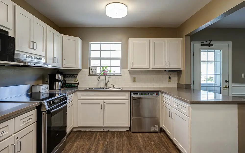 Modern kitchen with white cabinets, stainless steel appliances, a window above the sink, and brown countertops. Wooden flooring and neutral walls complete the space. Modern kitchen with white cabinets, stainless steel appliances, a window above the sink, and brown countertops. Wooden flooring and neutral walls complete the space.