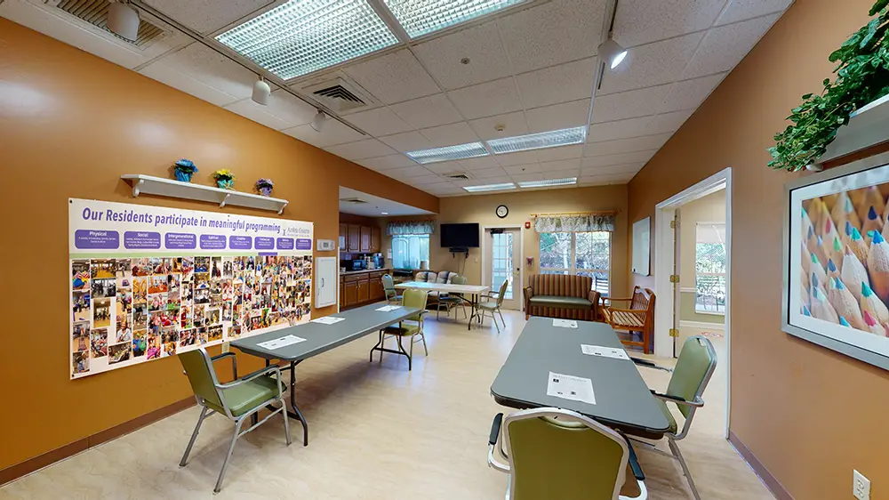 A community room with brown walls, tables, green chairs, a sofa, wall posters, a TV, and windows with curtains. A community room with brown walls, tables, green chairs, a sofa, wall posters, a TV, and windows with curtains.