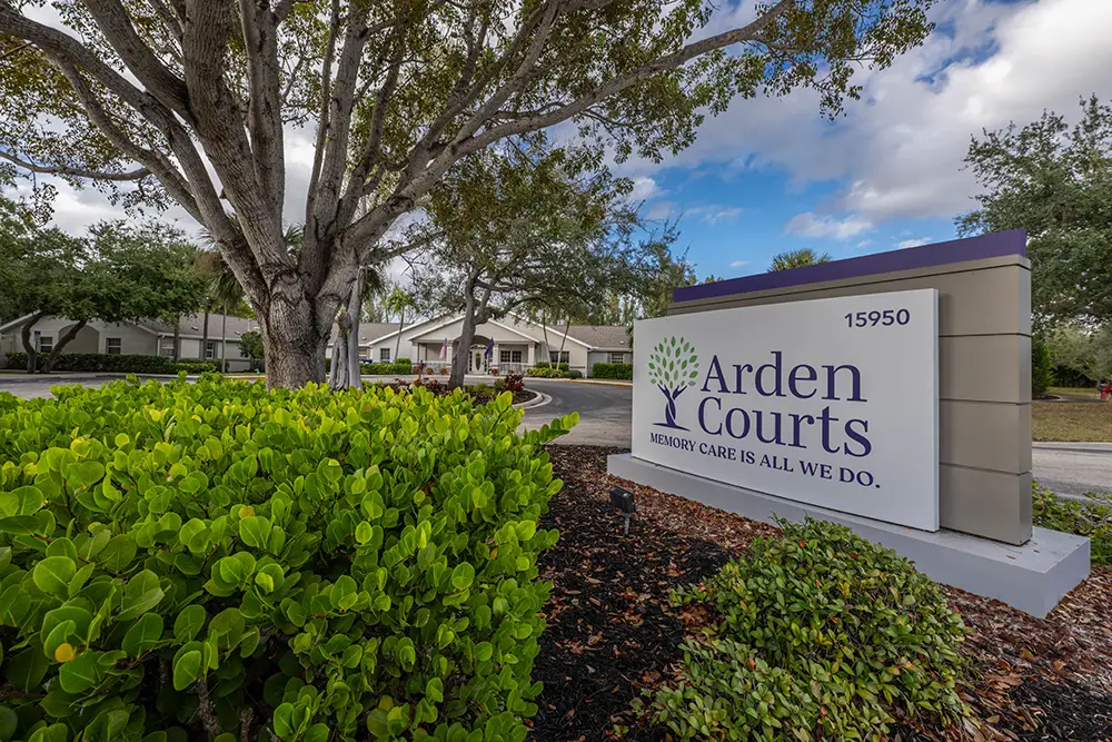 Entrance sign for Arden Courts, a memory care facility. Trees, landscaping, and a building are visible in the background under a partly cloudy sky. Entrance sign for Arden Courts, a memory care facility. Trees, landscaping, and a building are visible in the background under a partly cloudy sky.