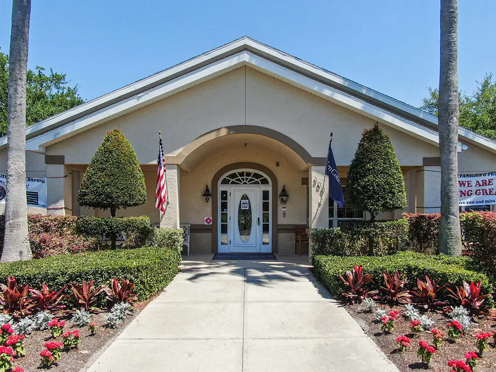 Single-story building in Largo with a front entrance, two flags, trimmed bushes, and landscaped plants lining the concrete walkway to Arden Courts memory care.