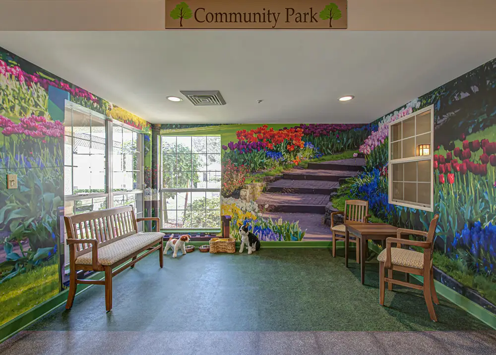A room with wooden benches, a table and chairs, pet toys, and a large wall mural depicting colorful flowers and a garden pathway.