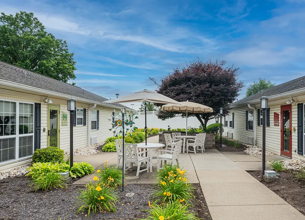 North Hills-11 A courtyard with patio furniture, umbrella, landscaping, and two single-story buildings under a blue sky with light clouds.