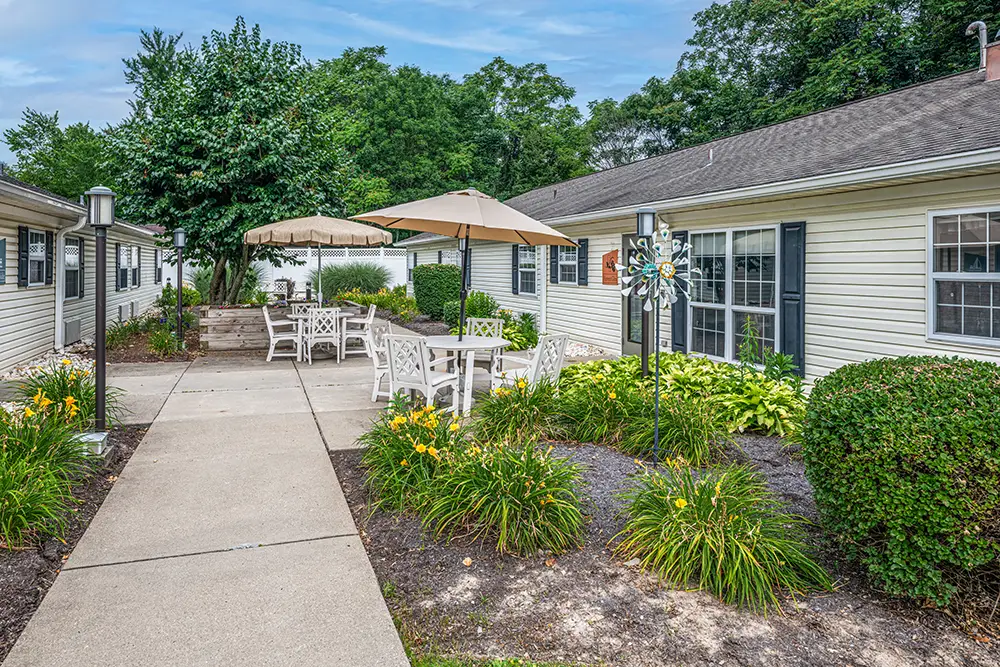 North Hills-3 A paved walkway runs between two single-story buildings with outdoor seating areas, umbrellas, and landscaped greenery.