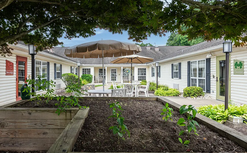 North Hills-9 A courtyard garden with young plants in a raised bed, patio tables and chairs under umbrellas, surrounded by single-story buildings.