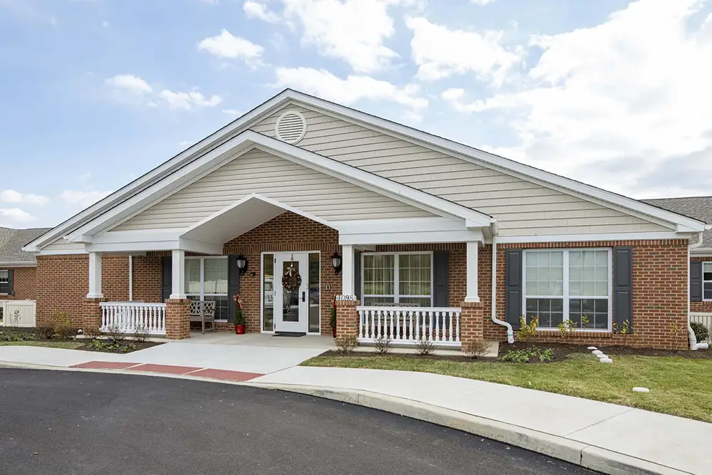 Single-story brick building with a covered entrance, white columns, and a small porch—Arden Courts of Old Orchard specializes in memory care amid landscaped grass and a convenient driveway out front.