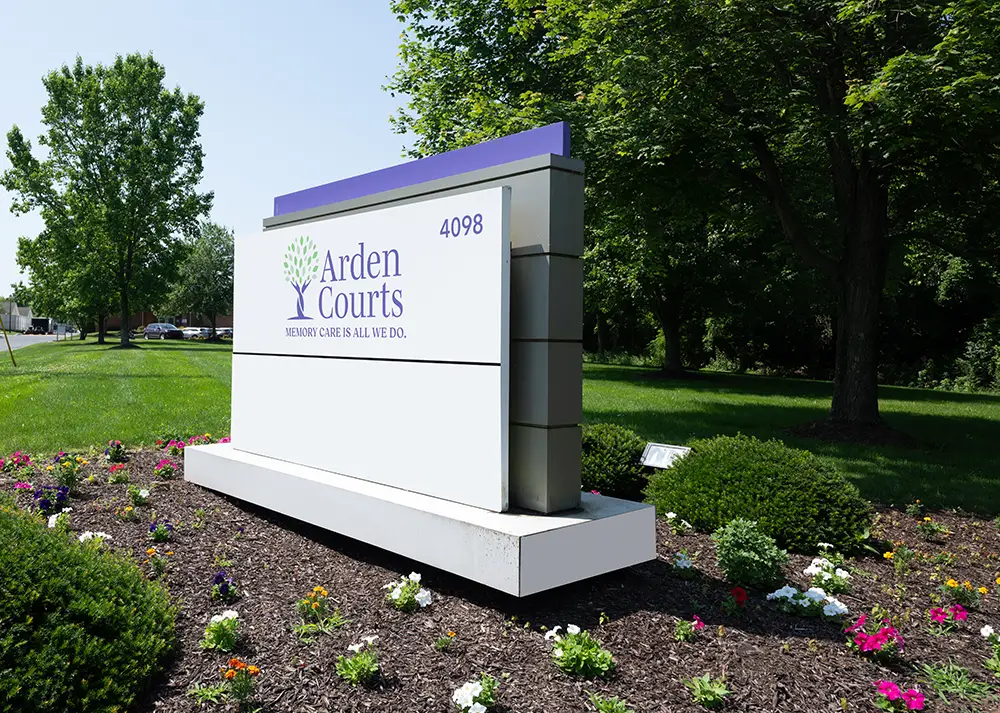 Orchard Signs-3 A sign for Arden Courts with the slogan "Memory Care Is All We Do" and the number 4098, surrounded by grass, trees, and flowers.
