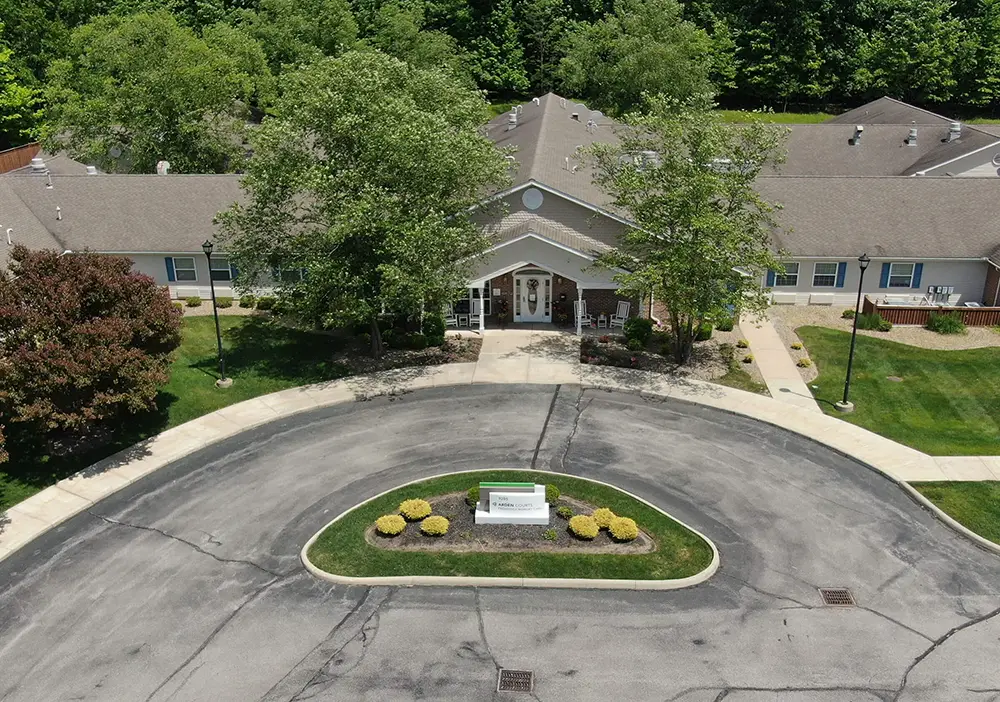 Aerial view of Arden Courts in Parma, a single-story memory care building with a circular driveway, landscaped center island, and surrounding trees.