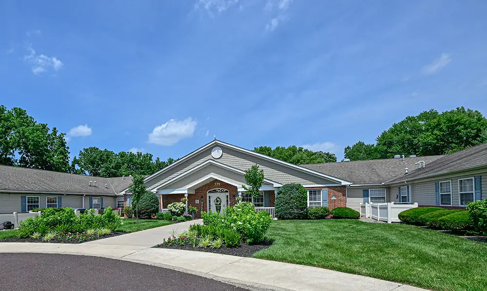 Sequence (1)Cedar Ridge signs-2 Single-story brick and siding building with a landscaped lawn, shrubs, and a circular driveway under a clear blue sky.