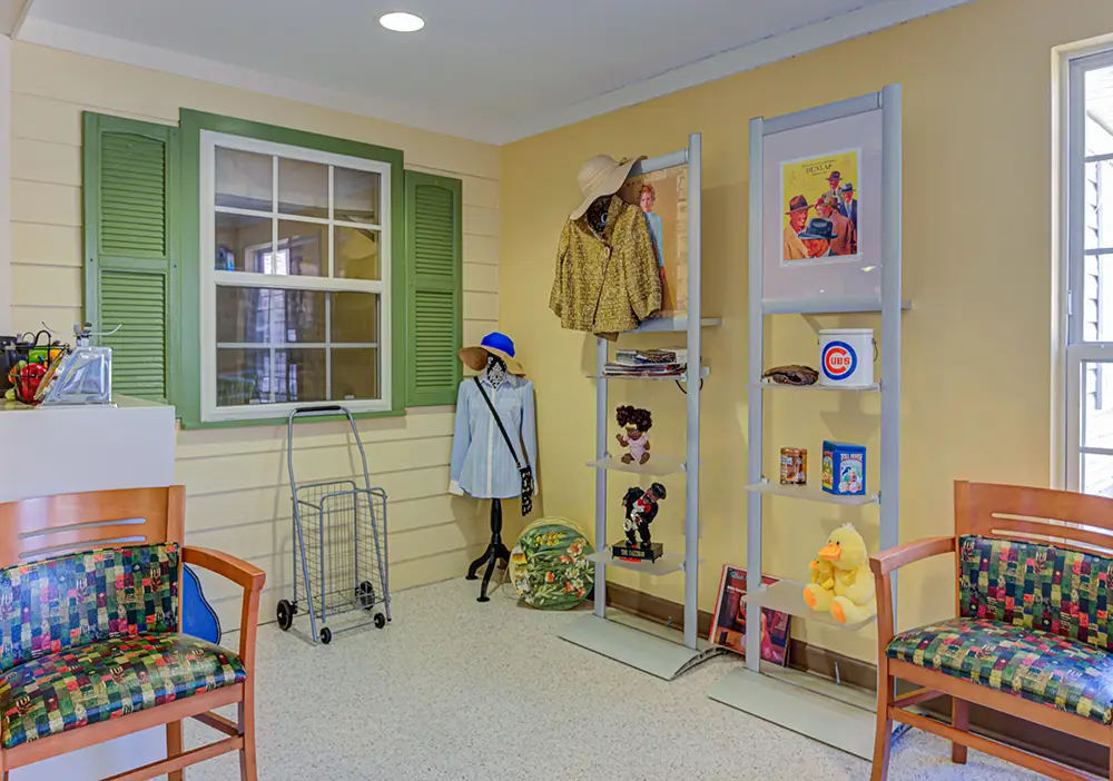A waiting area with colorful chairs, a decorative mannequin in a hat and coat, a shopping cart, and shelves displaying toys, books, and hats against yellow walls. A waiting area with colorful chairs, a decorative mannequin in a hat and coat, a shopping cart, and shelves displaying toys, books, and hats against yellow walls.