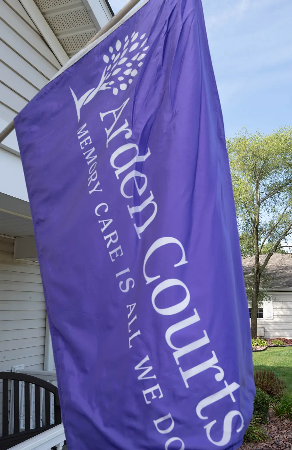 South Holland New photos01 A purple flag with white text reads "Arden Courts Memory Care is All We Do" next to a building and trees in the background.