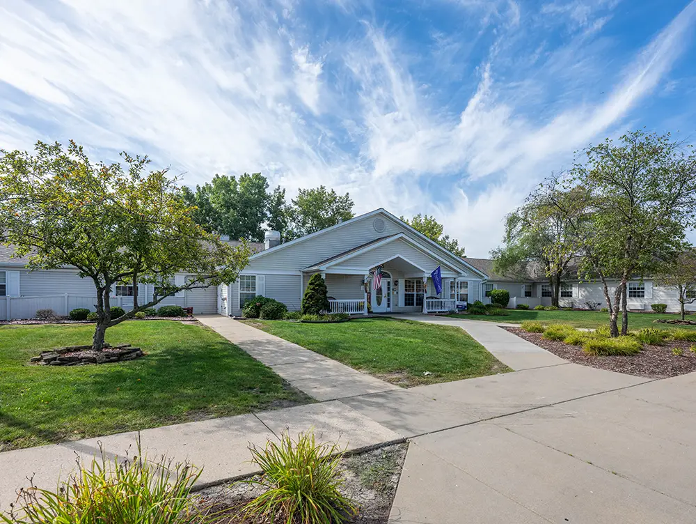 South Holland New photos02 Single-story white building with a covered entrance, American flag, green lawn, trees, and clear blue sky. Concrete walkways lead to the main entrance.