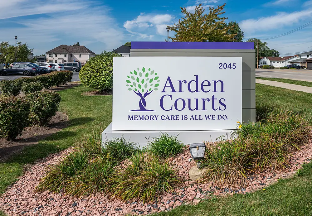 South Holland New photos03 A large sign in front of a care facility reads "Arden Courts, Memory Care is All We Do," with the address 2045 and a tree logo, surrounded by grass and landscaping.