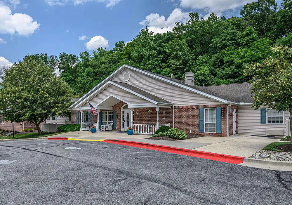 Single-story brick and siding building with a front porch, American flag, and surrounding trees in Towson, set against a partly cloudy sky—home to Arden Courts memory care community.