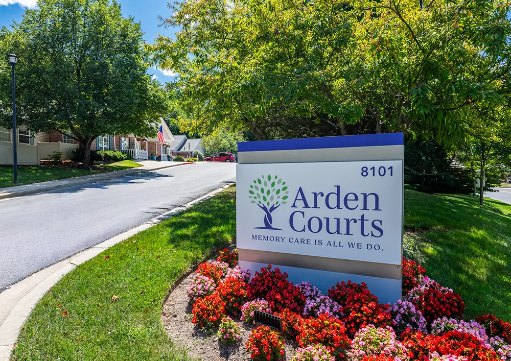 Towson A sign for Arden Courts Memory Care stands by a landscaped entrance with flowers, trees, and a driveway leading to residential buildings.