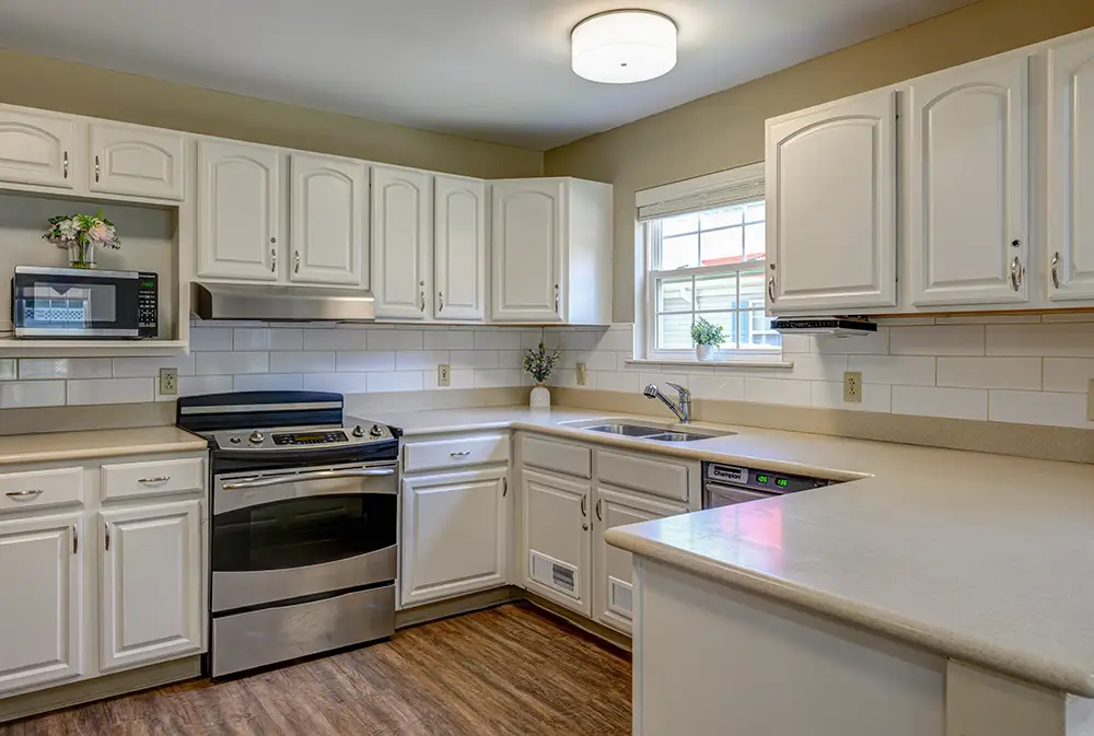 WAR_9088_89_90_91_92 Modern kitchen with white cabinets, stainless steel stove and dishwasher, microwave, tile backsplash, and a window above the sink.