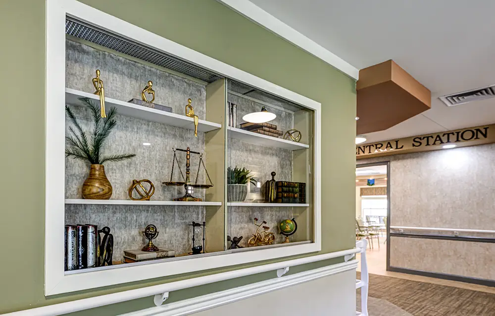 WAR_9178_79_80_81_82 A built-in wall shelf displays decorative items including books, statues, plants, a globe, and a set of scales in a hallway with green and beige walls.