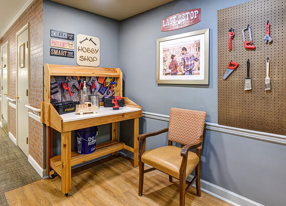 WAR_9198_199_200_201_202 Small woodworking station with toy tools on a bench, pegboard with hanging tools, a chair, and wall decorations in a hallway setting.