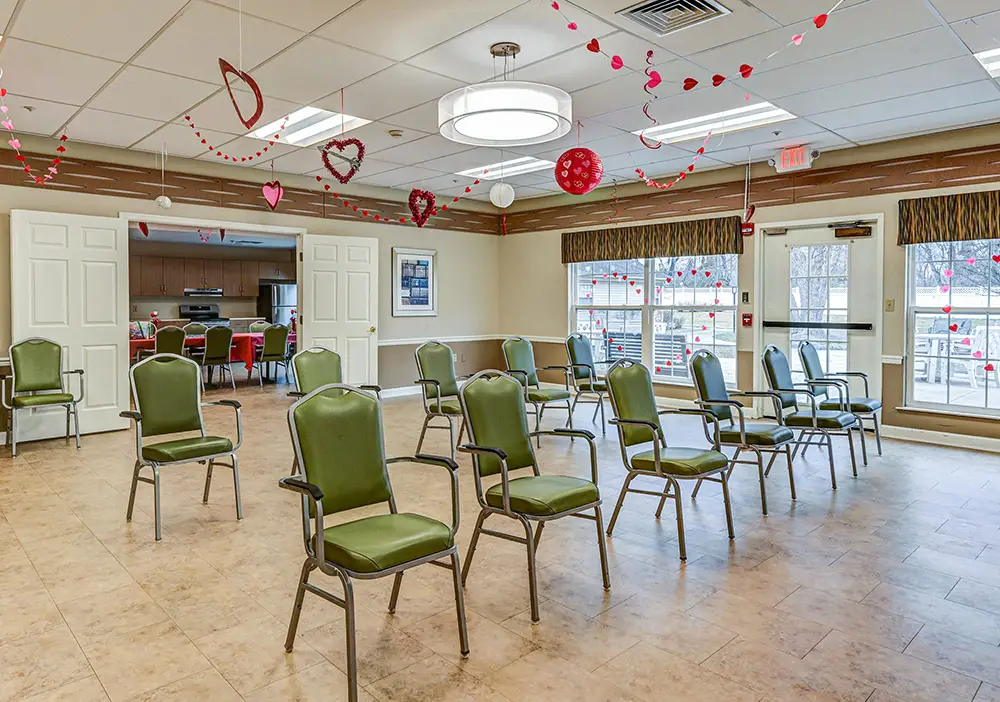 A community room with green chairs spaced apart, heart decorations hanging from the ceiling, and large windows letting in natural light. A community room with green chairs spaced apart, heart decorations hanging from the ceiling, and large windows letting in natural light.