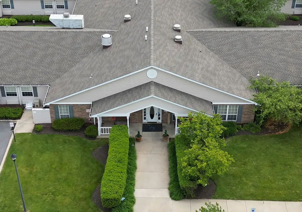 Aerial view of the front entrance of Arden Courts in Wilmington, a single-story brick building with a gabled roof, landscaped shrubs, and a concrete walkway designed for specialized memory care.