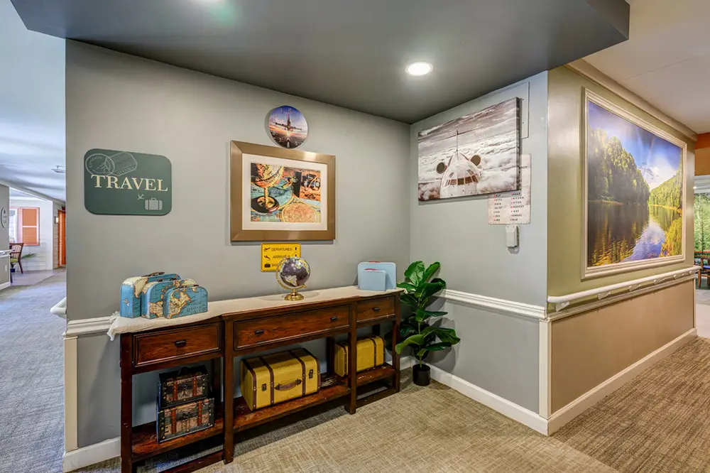 A hallway corner features a wooden console table with suitcases, a globe, and travel-themed wall decor, including photos, a sign, and a large framed landscape photograph.