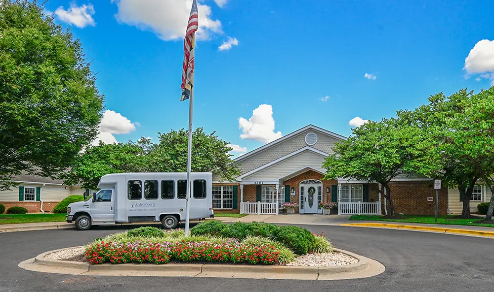 untitled-2021Kensington A white shuttle bus is parked in front of a single-story brick and siding building with a U.S. flag and landscaped flower bed in the foreground.